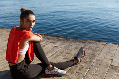 Full length portrait of young woman sitting on floor over sea