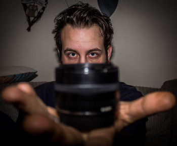 Portrait of man showing lens while sitting on sofa at home