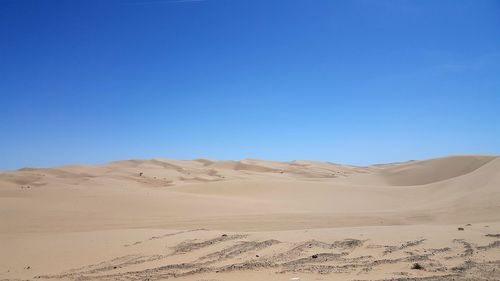 View of sand dunes in desert against clear blue sky