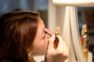 Side view of woman applying make-up in front of mirror at home