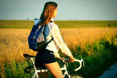 Woman sitting on bicycle against grassy field