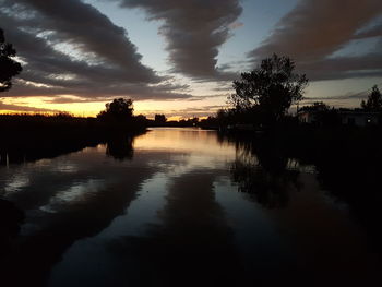 Silhouette trees by lake against sky during sunset