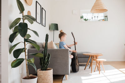 Young girl holding a guitar, musical instrument whilst sat at home