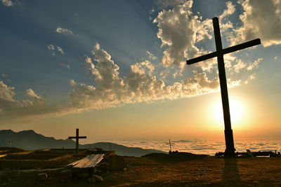 Silhouette crosses on mountain against cloudy sky during sunset