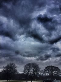 Silhouette of trees on field against storm clouds