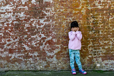 Full length portrait of girl standing against wall