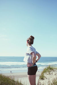 Rear view of woman standing on beach against sky