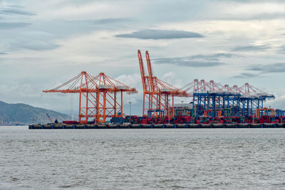 Cranes at commercial dock against sky