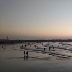 People on beach against clear sky during sunset