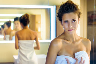 Young woman wearing towel standing in bathroom