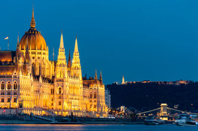 Hungarian parliament building by danube river against sky at dusk