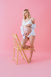 Portrait of young woman standing against pink background