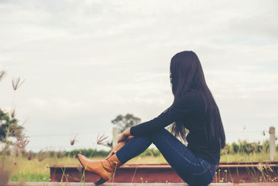 Side view of woman sitting against sky