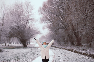 Happy young woman with arms raised standing at park during winter