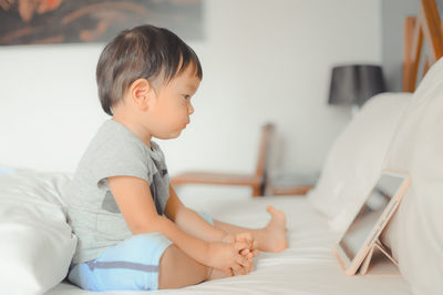 Side view of cute boy sitting on bed at home