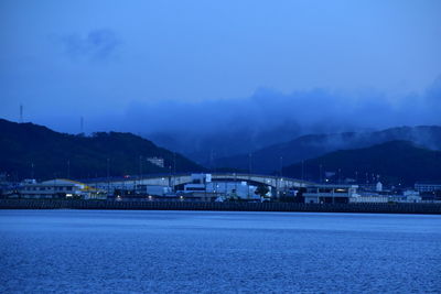 Illuminated city by mountains against sky at dusk