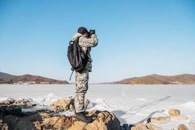 Rear view of person photographing on rock against clear sky