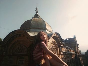 Portrait of young woman sitting on church against sky