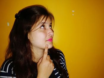 Close-up of thoughtful young woman against orange wall