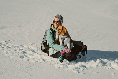 Smiling woman with dog sitting on snow covered land