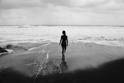 Rear view of man walking on beach against sky