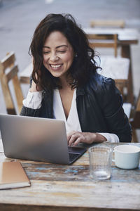 Cheerful woman using laptop while sitting at sidewalk cafe