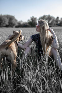 Young woman with dog sitting on grassy field against clear sky