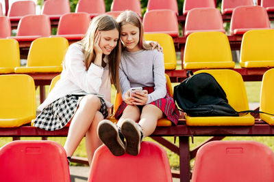 Two schoolgirls watch videos together on a smartphone in the school stands. 