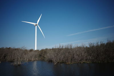 Wind turbines by lake against sky