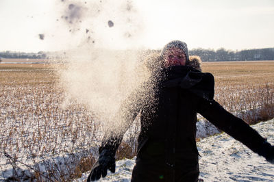 Young woman playing with snow while standing on field against clear sky