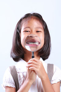 Portrait of schoolgirl showing teeth through magnifying glass against blue background