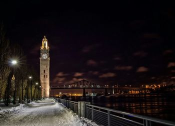 Illuminated clock tower by bridge over st lawrence river against sky at night during winter