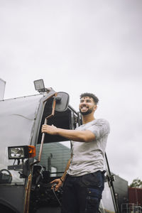 Smiling young construction worker looking away while standing at doorway of vehicle