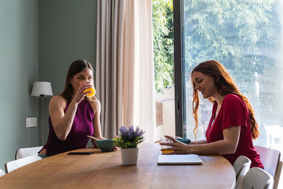 Young woman using phone while sitting on table