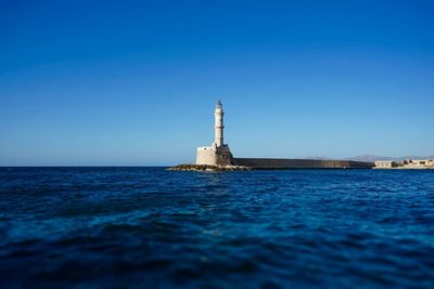 Lighthouse in sea against clear blue sky