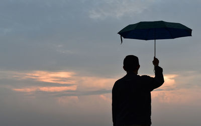 Silhouette man holding umbrella against sky during sunset