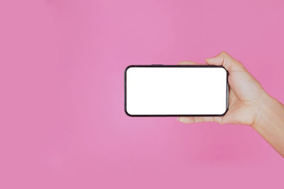 Low angle view of hand holding smart phone against pink background