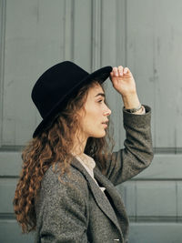Portrait of young woman looking away while standing against wall