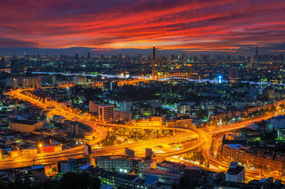 Aerial view of illuminated cityscape against cloudy sky at sunset