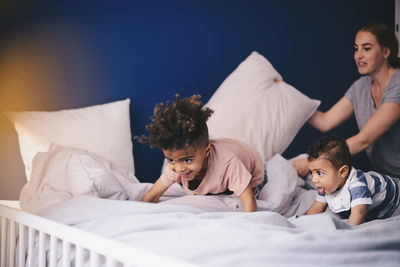 Mother holding pillow while children playing on bed at home