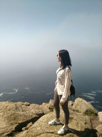 Woman standing on rock by sea against sky