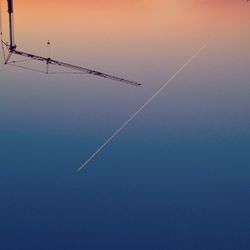 Low angle view of crane and vapor trail during sunset