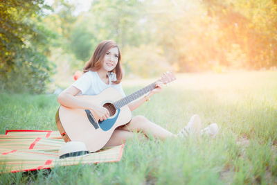Young woman with guitar on grassy field at park