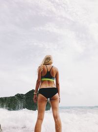 Rear view of woman standing by rock at beach against sky