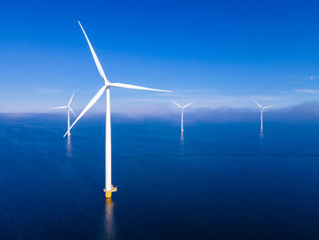 Wind turbines in sea against blue sky