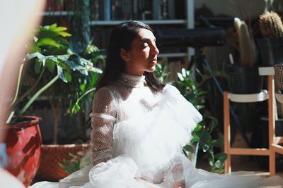 Woman in dress sitting against potted plants