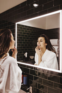 Mid adult woman looking in mirror while applying lip balm at hotel