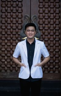 Portrait of young man standing against brick wall