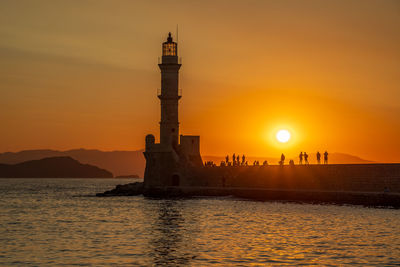 Lighthouse by sea against sky during sunset