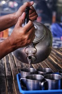 Cropped hand of person pouring water from teapot in glass